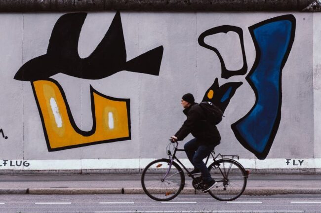 Fahrradtour Berlin: Mann fährt Fahrrad vor der BerlinerMauer